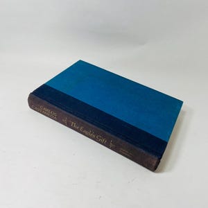 Op de afbeelding: Een hardcover boek getiteld "The Eagle's Gift" van Carlos Castaneda. Het boek heeft een blauwe kaft met een donkerblauwe rug en bruine randen. De titel en de naam van de auteur staan in gouden letters.