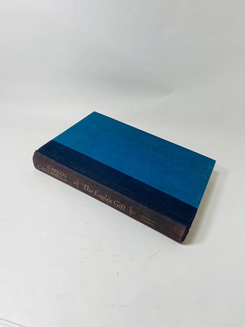 Op de afbeelding: Een hardcover boek getiteld "The Eagle's Gift" van Carlos Castaneda. Het boek heeft een blauwe kaft met een donkerblauwe rug en bruine randen. De titel en de naam van de auteur staan in gouden letters.