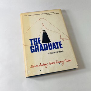 May include: A paperback book titled The Graduate by Charles Webb with a cream-coloured cover. The cover features a black silhouette of a graduate in a cap and gown positioned between two red line-drawn legs, with the text Now an Academy Award Winning Picture.