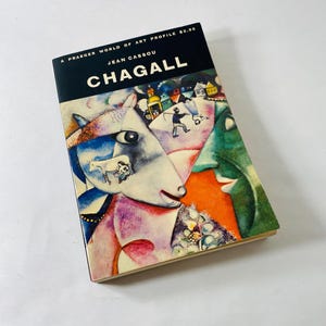 May include: A hardcover book titled "Chagall" by Jean Cassou. The cover features a colorful abstract painting with a white horse-like figure, buildings, and figures. The book is part of the "A Praeger World of Art Profile" series.