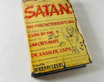 Könnte beinhalten: Ein Buch mit dem Titel "SATAN His Psychotherapy and Cure by the Unfortunate" von Jeremy Level. Das Cover ist vergilbt und zeigt roten Text und eine Zeichnung einer geflügelten Figur. Es scheint ein Roman zu sein.