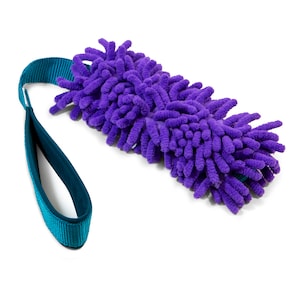 Puede incluir: Juguete para perro morado con una correa turquesa. El juguete está hecho de un material suave y peludo y está diseñado para ser interactivo para perros.