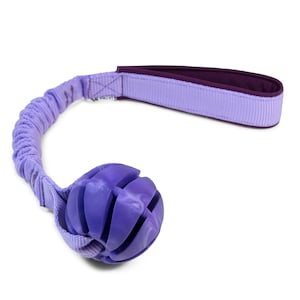 Puede incluir: Juguete para perro morado con un mango de cuerda y una pelota texturizada. La pelota tiene un patrón de mármol morado y blanco.