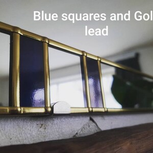 May include: A close-up of a decorative window frame with blue squares and gold lead. The frame is made of gold-colored metal and features rectangular blue glass panels. The text "Blue squares and Gold lead" is visible.