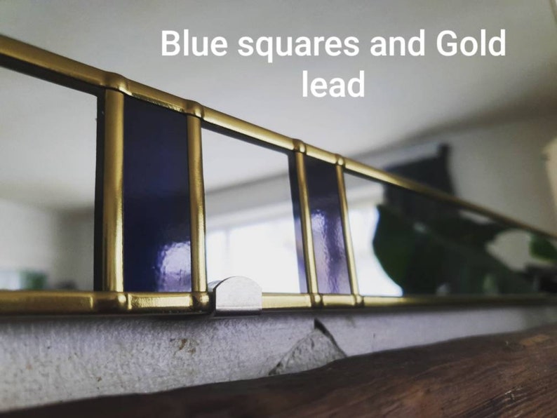 May include: A close-up of a decorative window frame with blue squares and gold lead. The frame is made of gold-colored metal and features rectangular blue glass panels. The text "Blue squares and Gold lead" is visible.