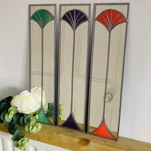 May include: Three stained glass mirrors with a mirrored surface and a decorative design. The mirrors are framed in silver and feature a green, purple, and orange stained glass design.