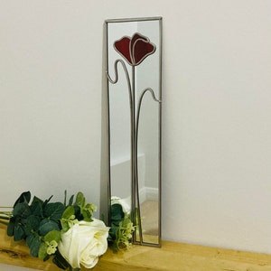 May include: A stained glass mirror with a red poppy design. The mirror is framed in silver and has a rectangular shape.