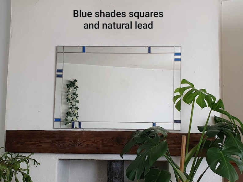 May include: Rectangular mirror with blue square accents and natural lead detailing. The mirror is mounted on a white wall above a wooden mantelpiece. The text "Blue shades squares and natural lead" is above the mirror.