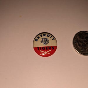 May include: A vintage Detroit Tigers button with a red and white design. The button features the team name and a tiger logo. A quarter is next to the button for size comparison.