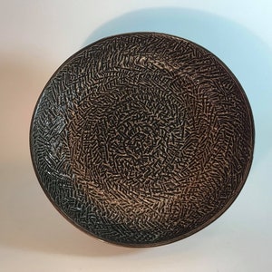 May include: A black ceramic bowl with a textured, swirling pattern. The bowl has a dark brown glaze and a slightly raised rim.
