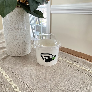 May include: A white paper cup with a black and green VR headset graphic and the number 10. The cup has a clear plastic lid.