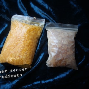 Puede incluir: Dos bolsas de plástico transparentes llenas de copos de cera amarilla y blanca. Las bolsas están sobre una superficie de terciopelo azul. + otros ingredientes secretos