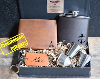 May include: A groomsmen gift set in a black box. The set includes a brown leather wallet, a brown leather keyring, a brown leather hip flask, and two silver shot glasses. The wallet, keyring, and flask are personalised with the name "Alex".