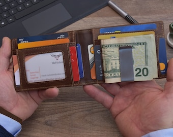 Puede incluir: Una cartera de cuero marrón con un clip para dinero. La cartera está abierta y tiene varias tarjetas y dinero en efectivo dentro. La cartera tiene una ventana para una identificación con foto.