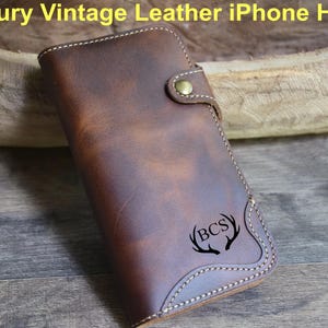 May include: A brown leather iPhone holder with a button closure and white stitching. The holder has a vintage look and features the text "A Luxury Vintage Leather iPhone Holder!" at the top and a "BCS" logo with antlers.