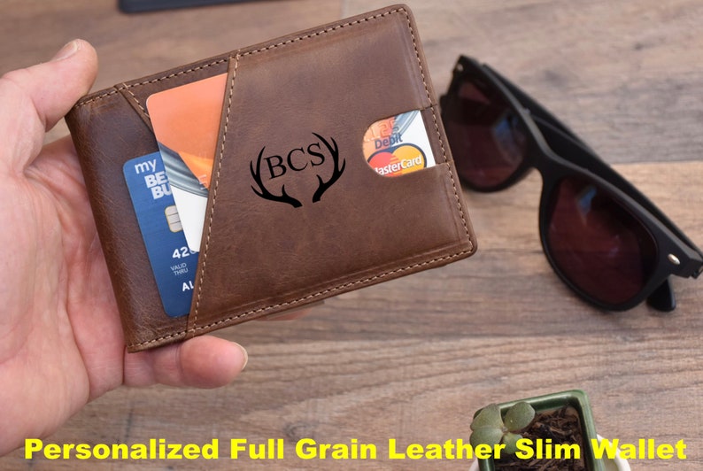 K&ouml;nnte beinhalten: Eine schlanke Geldb&ouml;rse aus braunem Leder mit einem personalisierten Monogramm "BCS" mit Geweih. Die Geldb&ouml;rse hat ein Kartenfach und einen Geldclip.