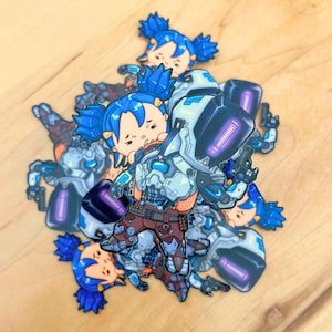 Könnte beinhalten: Ein Stapel bunter Aufkleber mit einem Comic-Charakter mit blauen Haaren und einem Roboter. Der Charakter trägt ein braunes und graues Outfit und hat einen überraschten Ausdruck. Die Aufkleber sind perfekt, um Laptops, Wasserflaschen oder anderen Oberflächen einen Hauch von Verspieltheit zu verleihen.