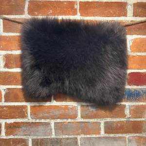 May include: A dark brown sheepskin rug with a soft, fluffy texture. The rug is hanging on a brick wall.