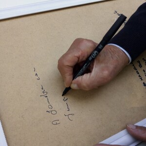 Puede incluir: Una persona firmando un documento enmarcado con un marcador negro. El texto en el documento dice "A Jourbre con" y "さしゃ".