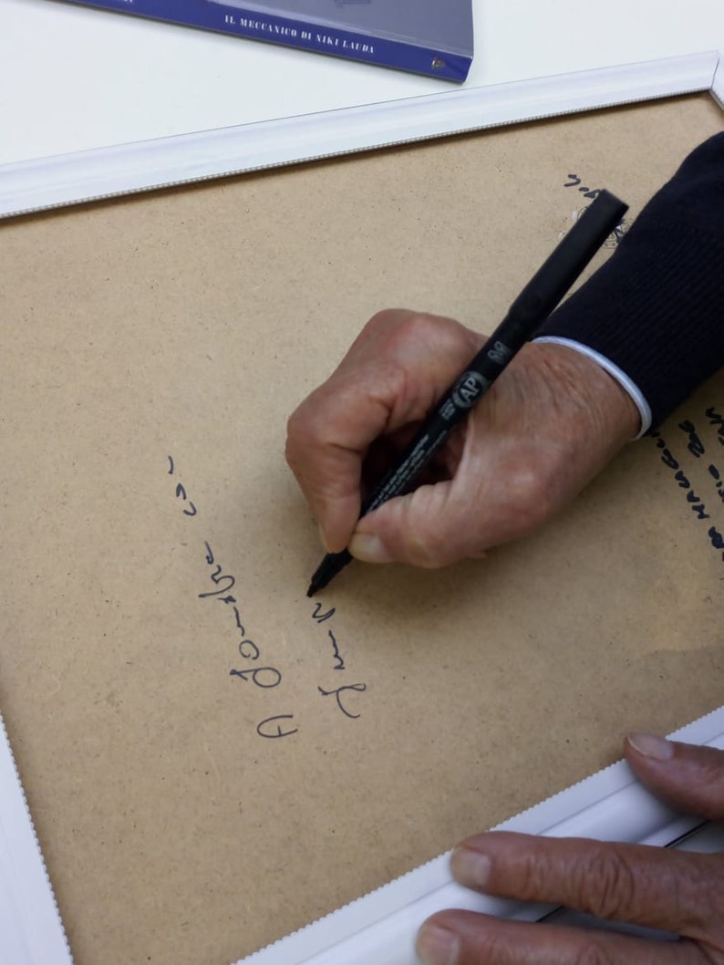 Puede incluir: Una persona firmando un documento enmarcado con un marcador negro. El texto en el documento dice "A Jourbre con" y "さしゃ".