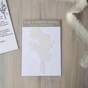 May include: White car window decal with a floral design. The decal is on a white background and is packaged in a clear plastic sleeve. The text "CAR WINDOW DECAL" is printed on the sleeve.