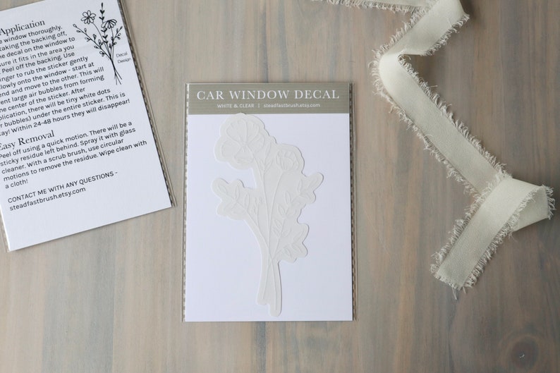 May include: White car window decal with a floral design. The decal is on a white background and is packaged in a clear plastic sleeve. The text "CAR WINDOW DECAL" is printed on the sleeve.