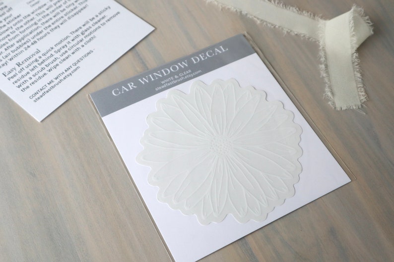 May include: White car window decal featuring a white flower design. The decal is on a white card with the text "CAR WINDOW DECAL" and "WHITE & CLEAN" printed on it.