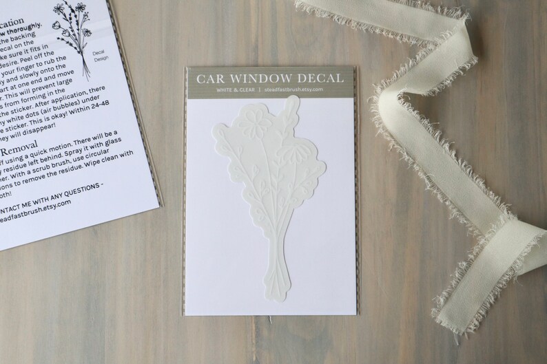 May include: White car window decal with a floral design. The decal is on a white background with the text "CAR WINDOW DECAL" and "WHITE & CLEAR" in black text.
