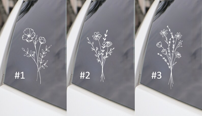 May include: Three white outline flower decals on a car window. The decals are numbered 1, 2, and 3. Each decal features a different floral design.