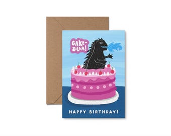 May include: A birthday card featuring a black monster with blue flames coming out of its mouth, sitting on top of a pink and white layered cake with red cherries. The card says "Cake-zilla!" and "Happy Birthday!"