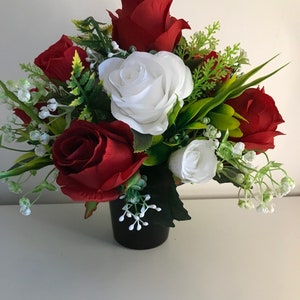 Könnte beinhalten: Ein künstlicher Blumenstrauß in Rot und Weiß in einer schwarzen Vase. Der Strauß besteht aus roten Rosen und weißen Rosen mit grünem Laub und kleinen weißen Blüten.