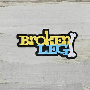 May include: A black and white sticker with the words "Broken Leg" in yellow and blue letters. A white bone is next to the words.