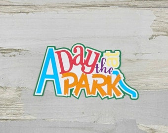 May include: A colorful, stylized logo with the text "A Day at the Park" in a green, blue, orange, red, and yellow color scheme. The logo is on a light wood background.