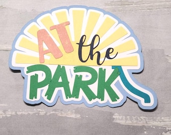 May include: A blue, yellow, and green paper craft with the text "AT the PARK" in a sunburst design.