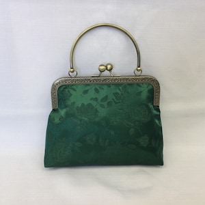May include: A green satin clutch bag with a floral pattern and a gold-toned metal frame.