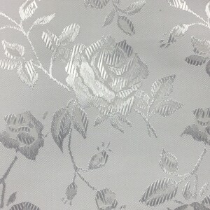Puede incluir: Tela blanca con un patr&oacute;n floral en relieve plateado. El patr&oacute;n presenta rosas y hojas.