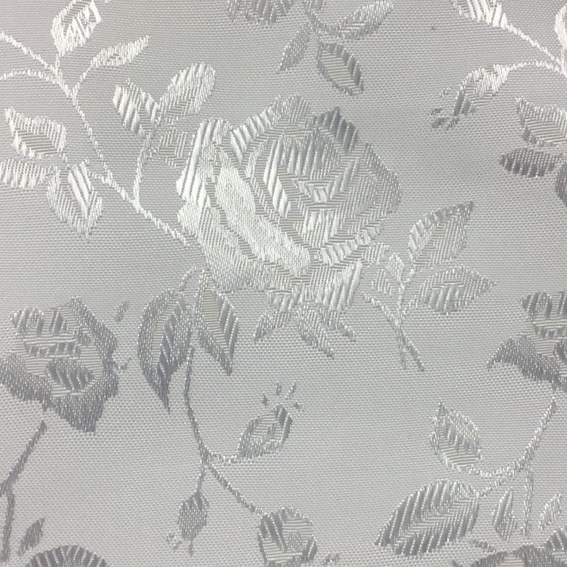 Puede incluir: Tela blanca con un patr&oacute;n floral en relieve plateado. El patr&oacute;n presenta rosas y hojas.