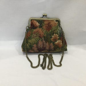 May include: A rectangular tapestry handbag featuring a botanical pattern of green leaves and rust-coloured floral elements. The bag has a bronze-toned metal frame with a kiss-lock closure and a matching bronze-toned metal chain shoulder strap.