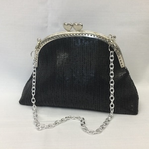 Puede incluir: Un bolso de noche negro de lentejuelas con una correa de cadena plateada y un cierre en forma de corazón.