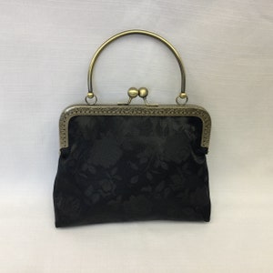 May include: A black satin clutch bag with a floral pattern and a gold-toned clasp and handle.