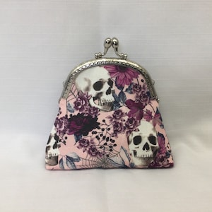 May include: A pink fabric coin purse with a silver clasp and a skull and floral print.