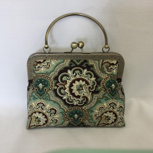 May include: A small, green and brown paisley patterned clutch purse with a brass frame and top handle.