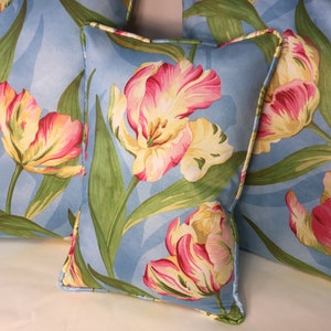 May include: Three blue throw pillows with a floral pattern of pink and yellow tulips on a light blue background.