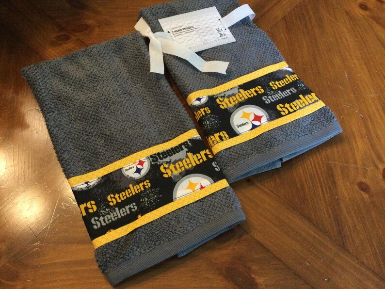 May include: Two gray kitchen towels with a yellow and black Steelers logo and the word "Steelers" repeated on the border.