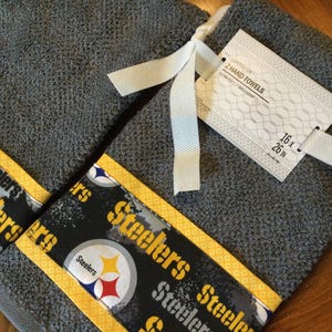 May include: Two gray hand towels with yellow trim and a black and white Steelers logo. The towels are 16 x 26 inches.