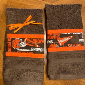 May include: Two brown hand towels with orange and black Cleveland Browns themed fabric trim. The towels are tied together with an orange ribbon.
