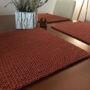 Könnte beinhalten: Vier gehäkelte Platzsets in Rostfarbe auf einem Holztisch. Die Platzsets sind aus einem dicken, strukturierten Garn gefertigt.