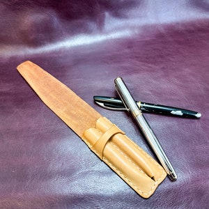 May include: A brown leather pen case with two pens inside. One pen is silver and the other is black with silver accents.