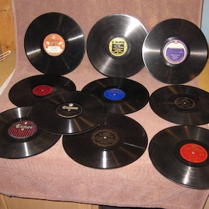 May include: A collection of ten black vinyl records with various labels and titles. The records are arranged in a semi-circle on a pink surface.