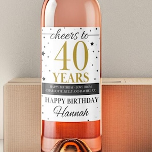 Könnte beinhalten: Eine Flasche Roséwein mit silbernem Verschluss und einem Etikett mit der Aufschrift "Cheers to 40 Years" mit dem Namen "Hannah" darunter. Die Flasche steht vor einer Pappschachtel.